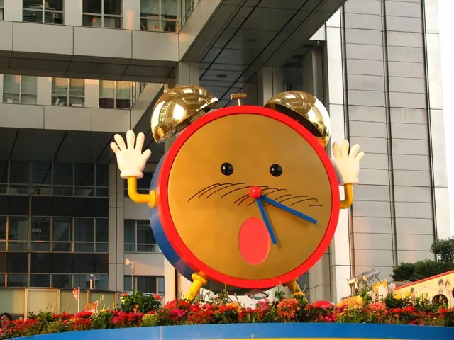 In the center of the image we can see an alarm clock. In the background there is a building. On the...